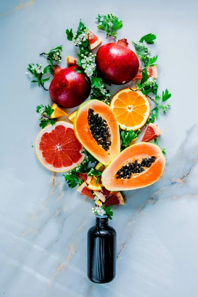 Свіжий зрізаний папайя зі стелями, гранатами, апельсинами біля чорної пляшки — стокове фото