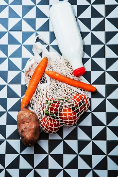 Worek netto z marchewką, mlekiem i pomidorami z ziemniakami na podłodze — Zdjęcie stockowe
