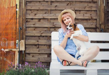 Arka bahçede ahşap kanepede oturan bir köpek ile genç kadın