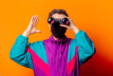 Yüz maskeli stil adamı ve turuncu arka planda dürbünlü 80 'lerin eşofmanı.