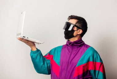 Beyaz arka planda dizüstü bilgisayarı olan 90 'ların ceketli ve yüz maskeli stil adamı.