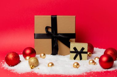 İki klasik Noel kutusunda kırmızı arka planda mücevherler ve kar var.