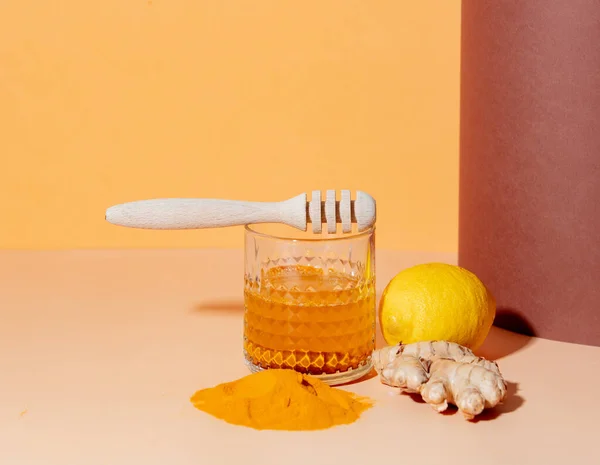 turmeric, honey, lemon and ginger next to a glass on a paper background
