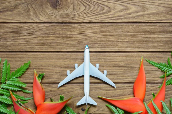 Vacation travel summer tropical Island weekend adventure trip background concept top view with copy space. Miniature toy plane with tropical flower and ferns on wooden background.