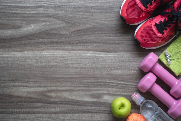 Ağırlık ve sağlıklı diyet aktif yaşam tarzı kavramı. Spor donatımı, halter, koşu ayakkabıları, yeşil ve kırmızı elma ve su ahşap arka plan üzerinde şişe.