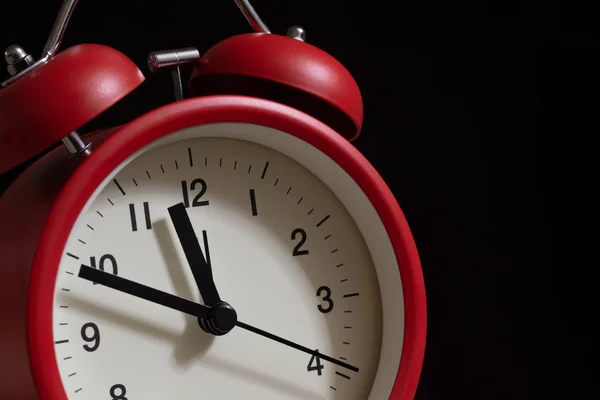 Red alarm clock close up. It\'s showing ten minutes to twelve o\'clock before alarm at twelve.