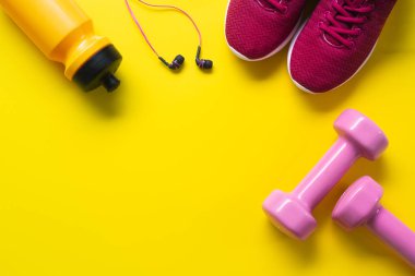 Düz kırmızı spor ayakkabı, pembe dambıl, kulaklık, şişe suyu sarı zemin üzerinde yatıyordu. Aktif sağlıklı yaşam tarzı, egzersiz, kilo ve diyet kavramı.