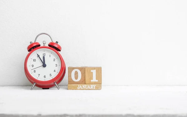 Close up of wooden calendar date 01 January with red alarm clock on white grunge wood table with copy sapce. New Year\'s Eve 1 January date end of year start the New Year new era.