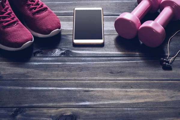 Fitness, healthy and active lifestyles Concept, dumbbells, sport shoes,  smartphone with earphone on wood background. copy space for text.