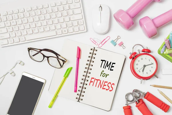 Time for Fitness active healthy lifestyle background concept. Flat lay of office workspace desk with keyboard and mouse, office stationery, alarm clock, dumbbells and workout equipment, with text time for fitness on notebook.