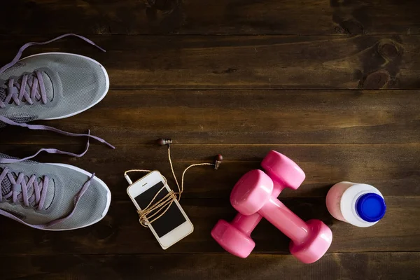 Fitness, healthy and active lifestyles Concept, dumbbells, running shoes, bottle of milk, smartphone with earphone on wooden background. Top view with copy space for text.