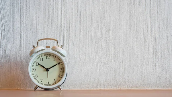 White vintage alarm clock displaying 10:10 am or pm on wooden ta