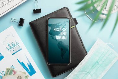 Corona virüsünden sonra işler normal. 19 salgın geçmişi var. Ev ofisinin çalışma masasında defter ve tıbbi yüz maskesi olan akıllı telefon..