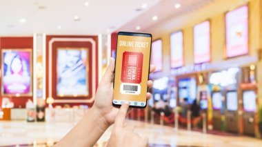 Mockup cep telefonu kullanıcısı, sinema biletleri almak için akıllı telefonu kullanıyor. Sinema salonundaki bilet satışlarının bulanık görüntüsü var. Grafik ikonu, online rezervasyon ve ödeme konsepti.