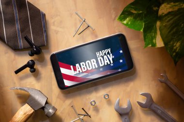 İşçi Bayramı soyut geçmiş konseptin kutlu olsun. Mutlu İşçi Bayramı metni ve iş adamının çalışan ahşap masa geçmişi üzerine temel çalışma araçları olan düz model akıllı telefon..