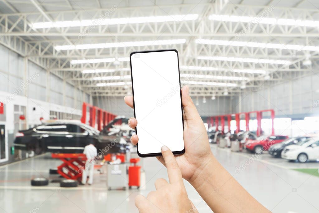 Mock up smartphone for automobile online service mobile application. Mockup blank white screen mobile phone with finger point and touch on touchsreen in  Auto repair shop.