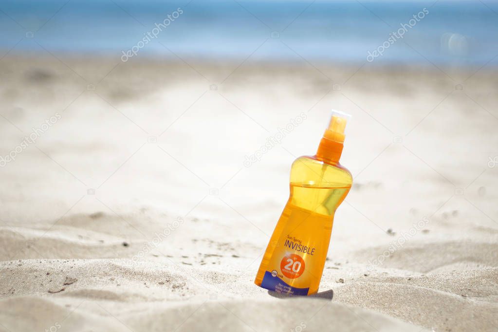 Sun spray, cream on the sandy beach with blurred sea background - summer beach concept