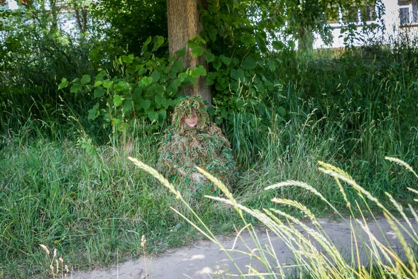 Genç bir kadın, kamuflaj kıyafeti giymiş, iplikçiklerden, askeriyeden, kikimora 'dan yapılmış, bir ağacın altında, çimenlerin altında oturan, çim, kurs, sınıf, yaz, orta boy, açık hava, yatay fotoğraf,