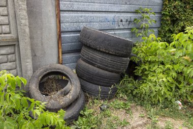 Eski lastik lastikler beton bir çitin altında yığılmış, eski lastikler, kel lastikler, yığının içinde yatıyor, çöp, yabani otlar, yaz, eko, yatay fotoğraf, lastik tekerlek, atık, araba