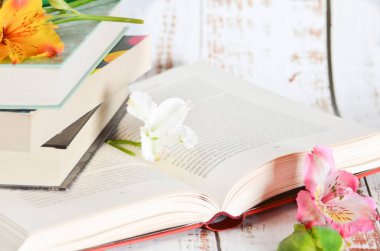 Üç kapalı kitabı olan açık kitap ve çiçekler.