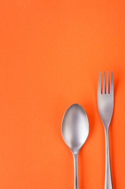 Turuncu arka planda çatal ve kaşık, kopya alanı ile seyrek kompozisyon. Yemek teması şablonu ve arkaplan