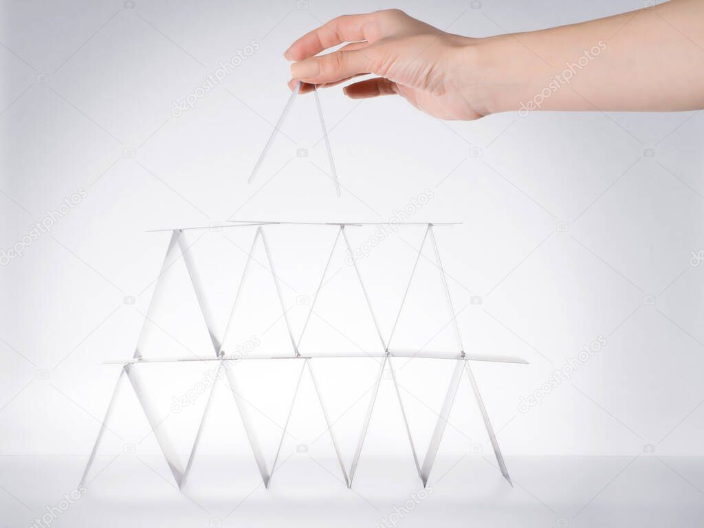 House of cards construction. Woman hand placing the upper section of the structure. Side view isolated on gray, clipping path included