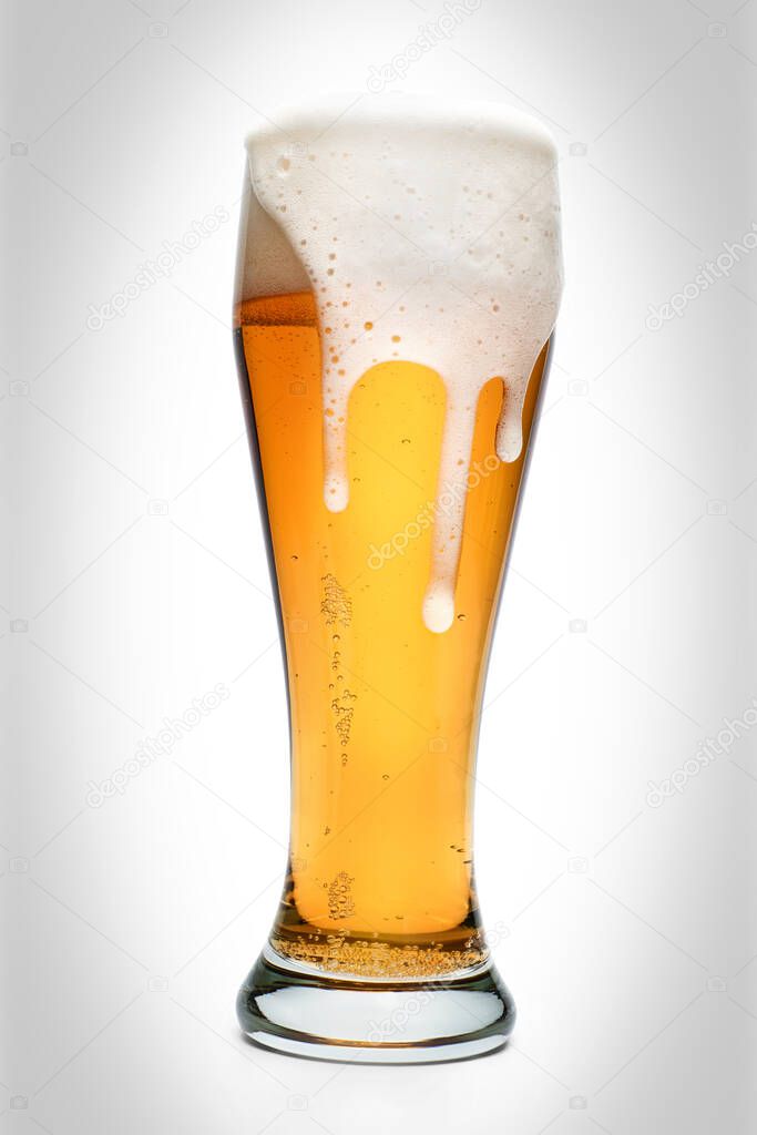 Large drinking glass full of amber beer with rich spilled foam. Isolated on white