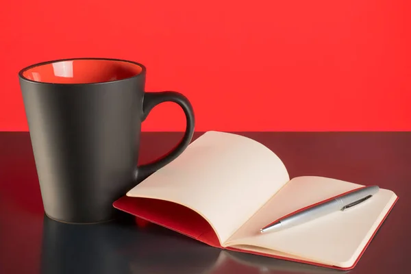 咖啡杯 打开的笔记本 黑色桌子上的钢笔和红色背景 — 图库照片