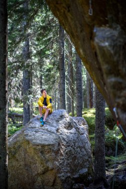 İskandinav orman içinde bir kaya üzerinde oturan genç gezgin adam. Kuzey Avrupa hedef. Seyahat kavramı.