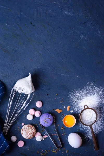 Bakery ingredients - flour, eggs, sugar, yolk, macaroni dessert on blue table. Sweet pastry party baking concept. Flat lay, copy space, top view.