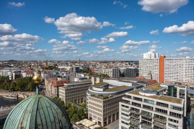 Berlin 'in panoramik manzarası çatıları, nehri ve katedral kubbesini gösteriyor. Şehir bulutlarla dolu bir gökyüzünün altında uzanıyor..