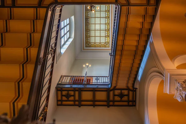 Vitraylı camla çerçevelenmiş merdiven manzarası. Lambalar tarihi iç tasarımı vurgular.