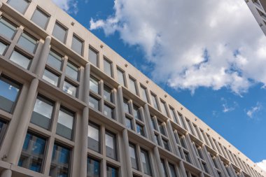 Tekrarlanan pencere ve sütunları ile modern mimari parlak gökyüzü ile buluşuyor. Bardaktaki yansımalar simetriyi ve kentsel tasarımı vurguluyor.