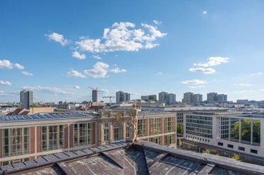 Yukarıdan manzaralı, ön planda çatısı olan bir heykel. Modern bloklar ve turnalar ufka kadar uzanıyor..