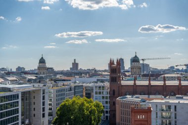 Berlin 'in çatısı. İkiz kilise kubbeleri ve kırmızı tuğlalı mimarisi var. Ufuk çizgisinde vinçler ve modern binalar yer alıyor..