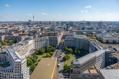 Berlin 'in televizyon kulesi ve şehir merkezindeki eğri binalarla hava görüntüsü. Yeşil alanlar ve sokaklar modern manzarayı çerçeveliyor.