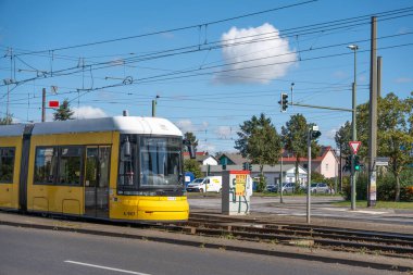 Almanya 7 Eylül 2025. Sarı bir tramvay yerleşim alanından geçiyor. Arka planda ağaçlar, evler ve mavi bir gökyüzü var..