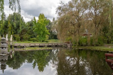Taş fenerli bir gölet ve ahşap köprü yemyeşil ağaçlarla çevrilidir. Durgun sudaki yansımaları bir ayna etkisi yaratıyor..