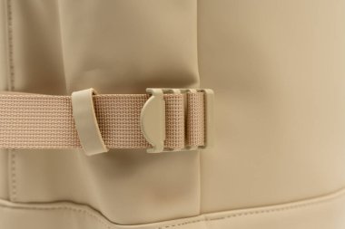Beyaz arka planda bej bir sırt çantasının tokasının detaylı görüntüsü. Madde dokusunu ve kopça tasarımını vurgular.