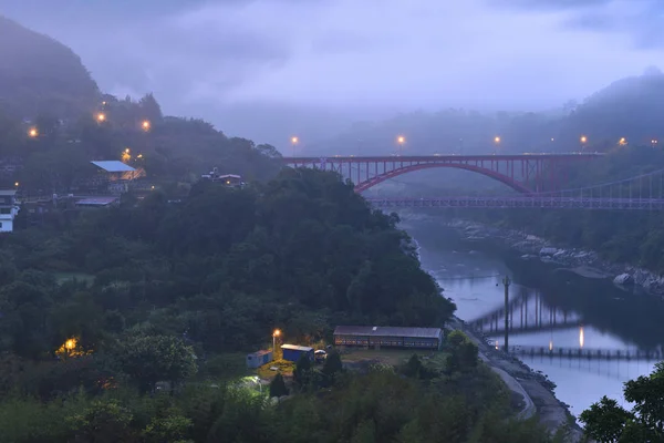 bridge and buildings in green mountainous landscape at dusk