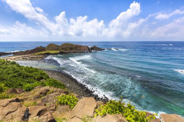 bulutlu gökyüzü altında okyanus kıyısında kayalar ve yeşillik