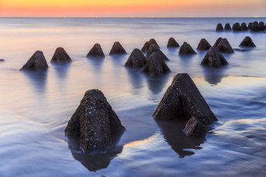 gün batımı gökyüzü ile okyanus suyunda piramit şeklinde kayalar