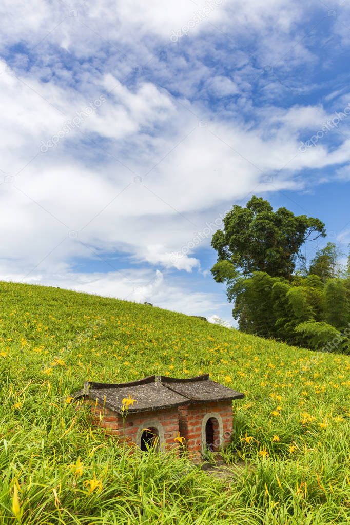 small brick huts on green field with yellow flowers under cloudy sky