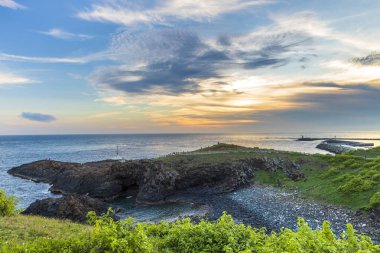 gün batımı bulutlu gökyüzü ile okyanus kıyısında yeşil tepe