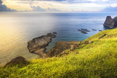 gün batımı bulutlu gökyüzü ile okyanus kıyısında yeşil tepe