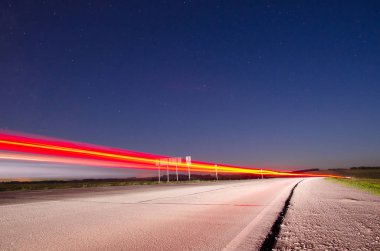 Asfalt yolun üzerinden araba hızda uzun pozlama üzerinde geçen ışık ile gece şehir dışında