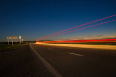 Asfalt yolun üzerinden araba hızda uzun pozlama üzerinde geçen ışık ile gece şehir dışında