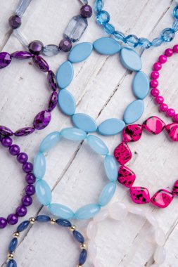Birkaç güzel bilezik, boncuk ve taş mavi, pembe ve mor beyaz ahşap zemin üzerinde
