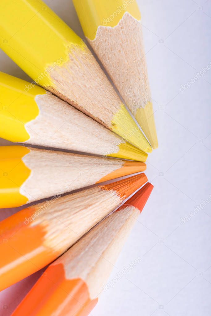 Macro photograph of several sharpened pencils of yellow and orange color on a white background