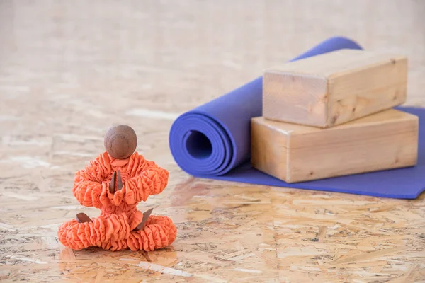 Figurine in orange clothes sitting in a yoga pose with a purple mat for exercise and meditation